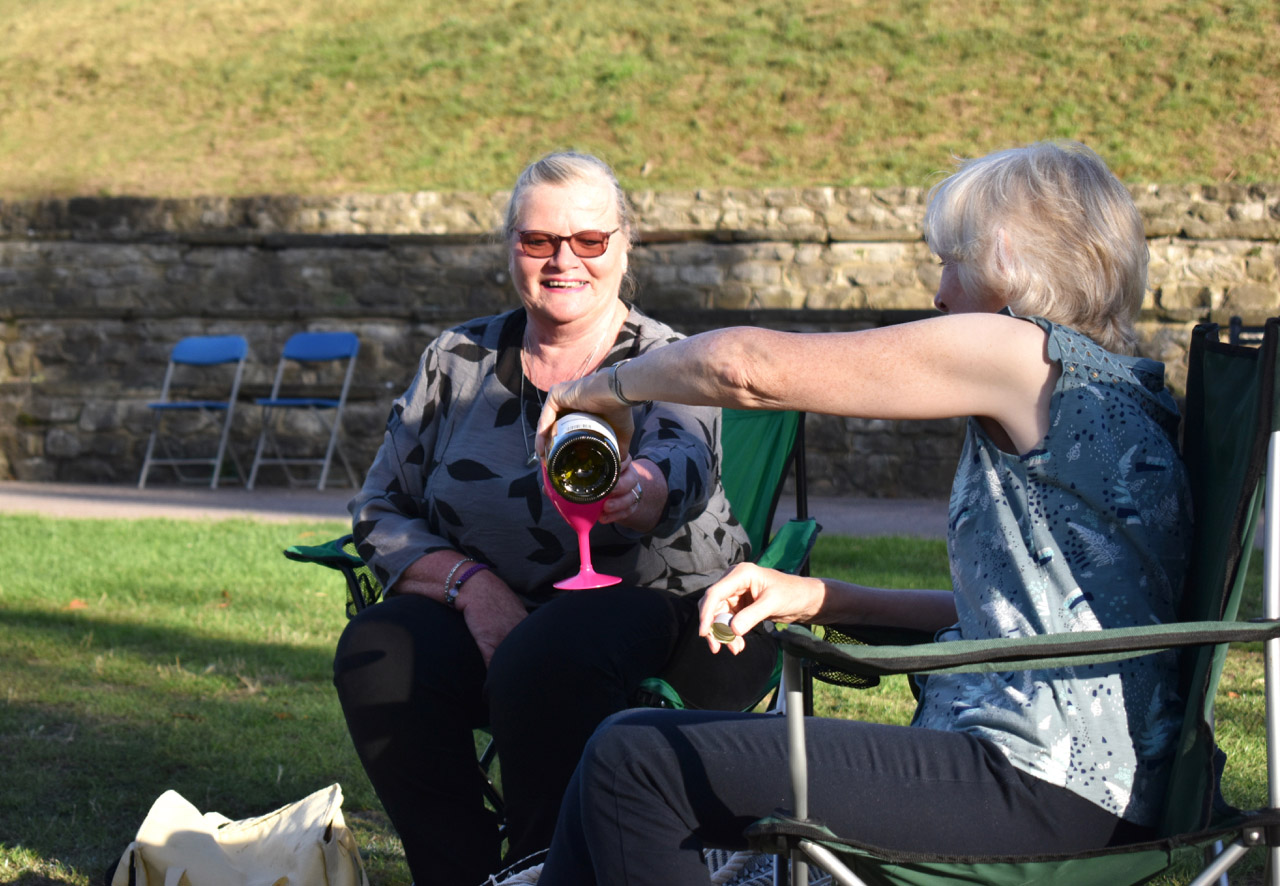 Women drinking wine at outdoor comedy event.