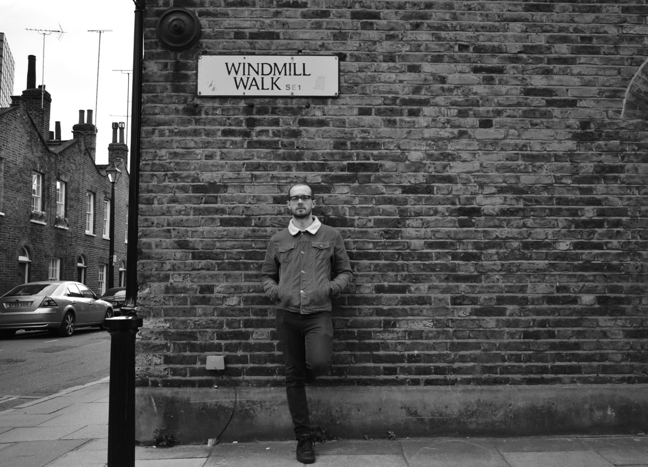 Man against wall underneath street sign.