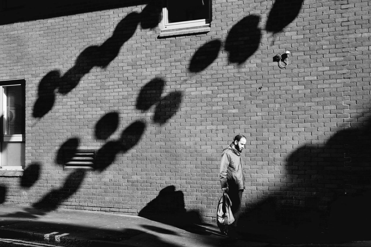 Image of man walking in street, background of ball-shaped shadows.