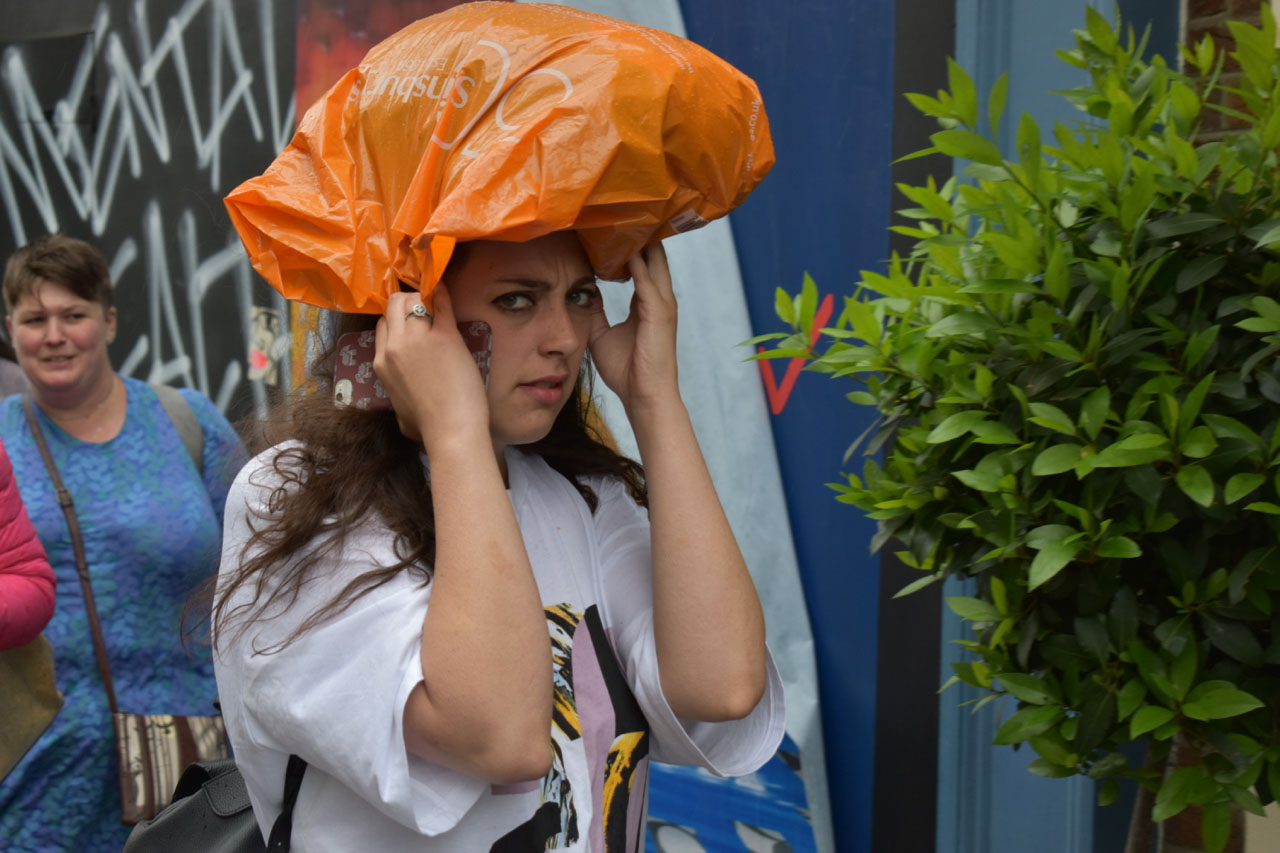 Image of a woman using an orange carrier bag to protect herself from rain.