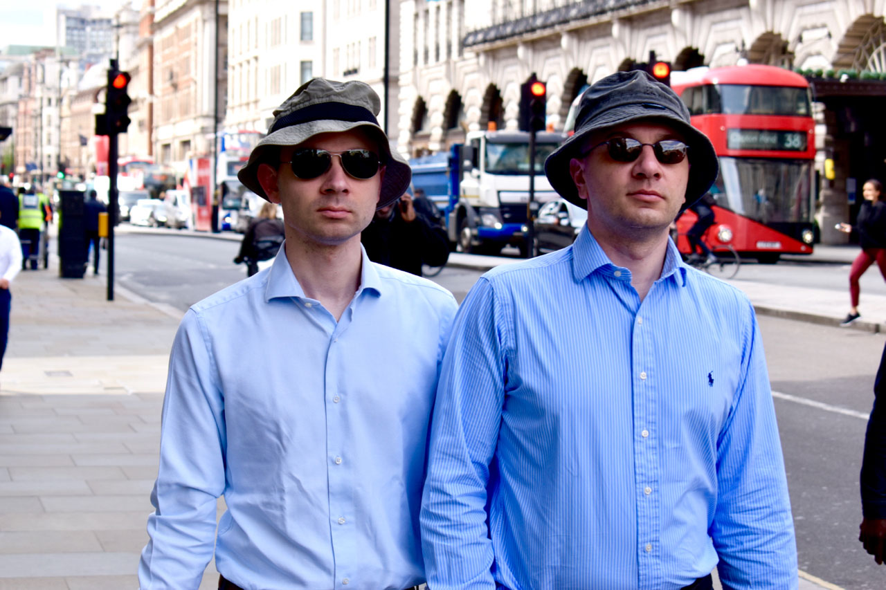 Image of two men wearing identical hats and blue shirts.