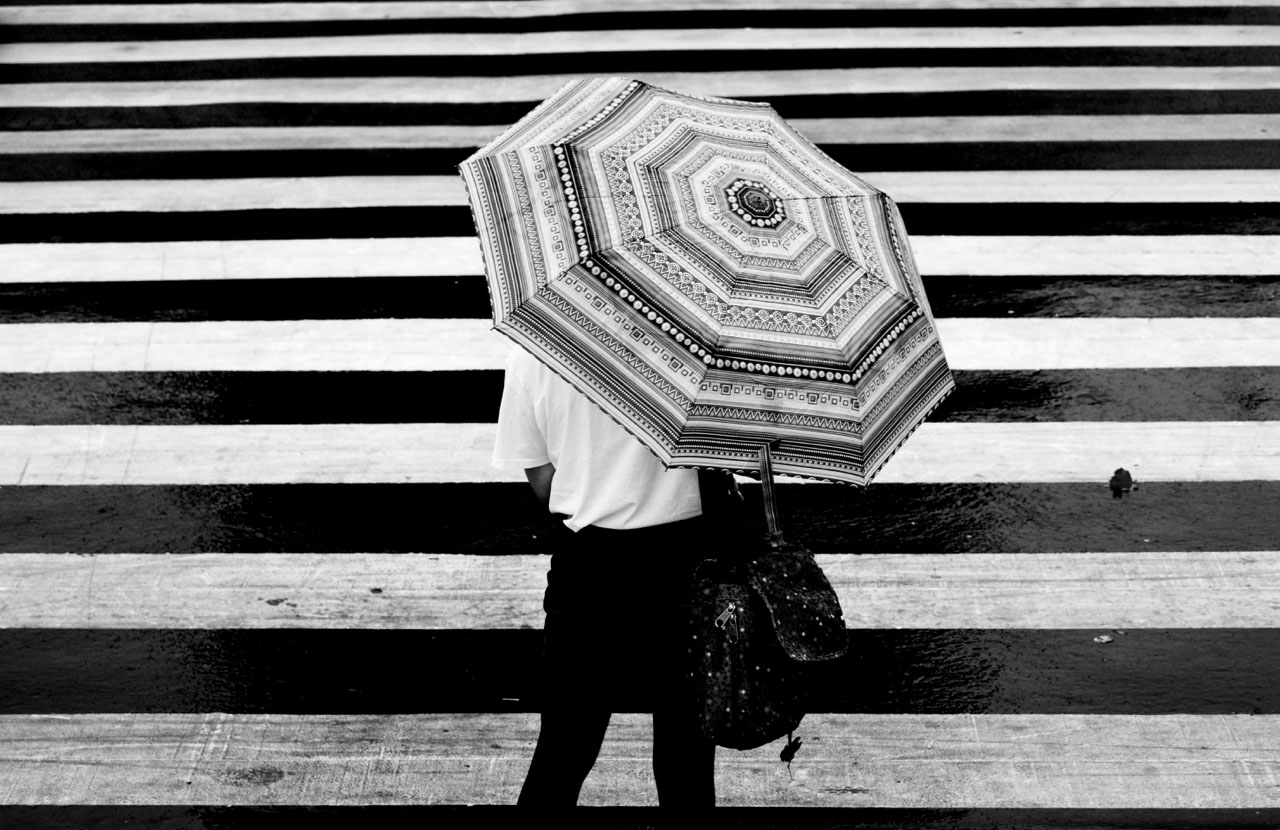 Image of zebra crossing and umbrella with similar pattern from behind.